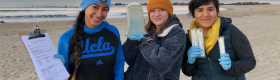 Student researchers on the beach hold up water samples for the camera