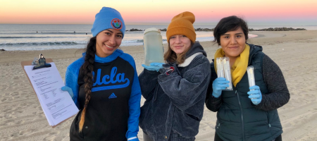 Student researchers on the beach hold up water samples for the camera