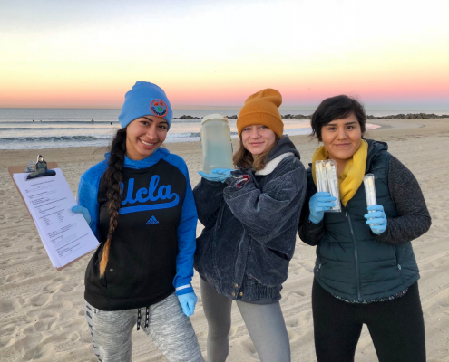 Student researchers on the beach hold up water samples for the camera