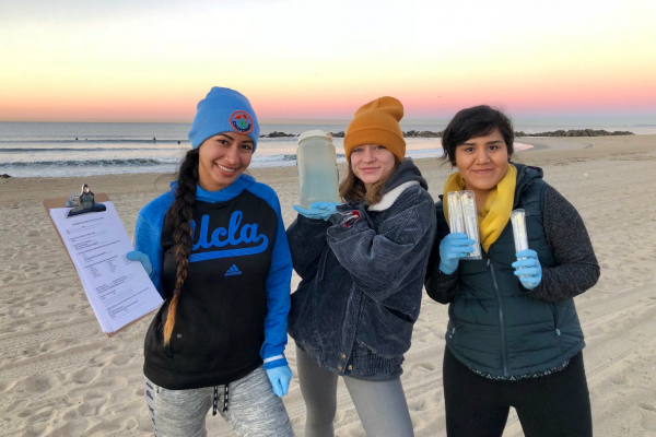 Student researchers on the beach hold up water samples for the camera