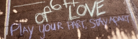 A photo of the sidewalk with chalk that says "Play your part, stay apart"