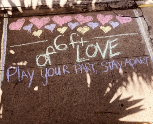 A photo of the sidewalk with chalk that says "Play your part, stay apart"