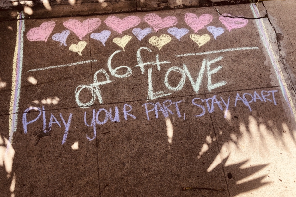 A photo of the sidewalk with chalk that says "Play your part, stay apart"