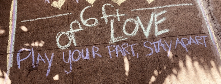 A photo of the sidewalk with chalk that says "Play your part, stay apart"