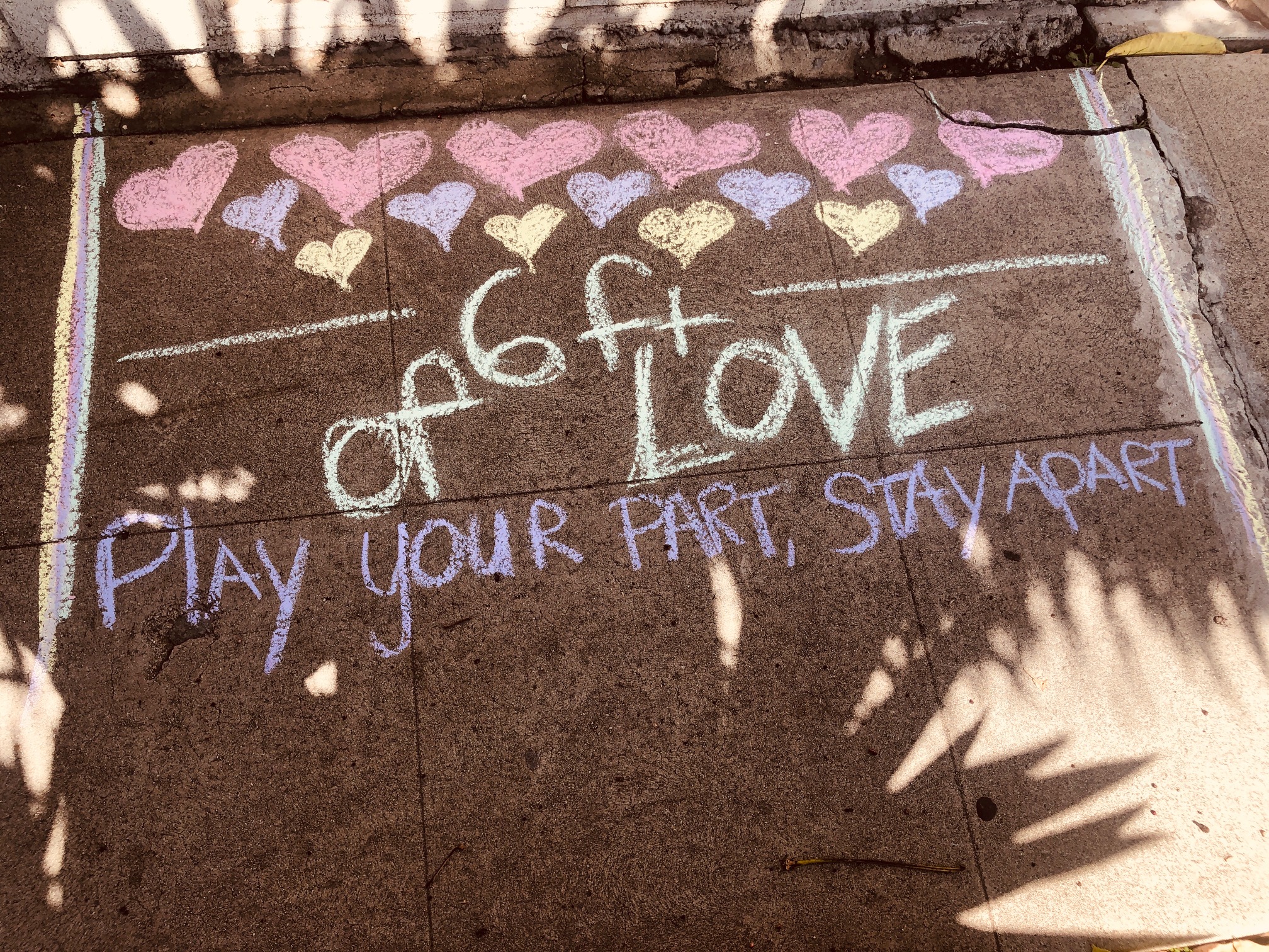 A photo of the sidewalk with chalk that says "Play your part, stay apart"