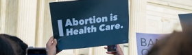 Image of a person in front of the U.S. Capitol holding a sign that reads "Abortion is health care"