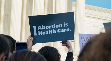 Image of a person in front of the U.S. Capitol holding a sign that reads "Abortion is health care"
