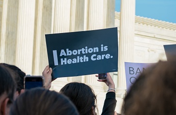 Image of a person in front of the U.S. Capitol holding a sign that reads "Abortion is health care"