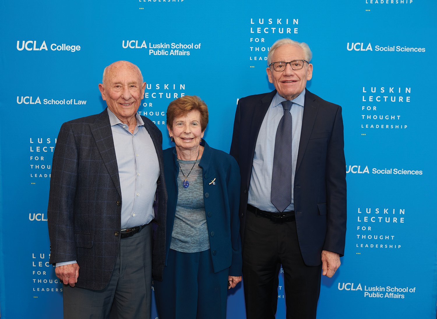 Image of Meyer and Renee Luskin standing with Bob Woodward in front of a blue background.