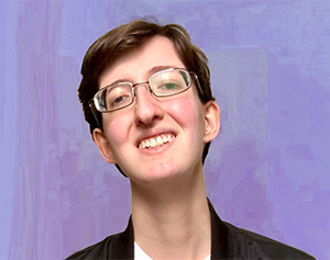 Photo of Christopher, a white genderqueer man with short brown hair, small-framed glasses, a white t-shirt, and a black bomber jacket with a trans pride pin, smiles to the camera in front of a lavender background.