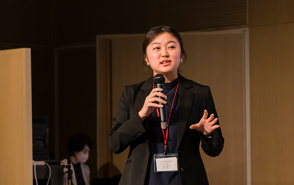 Kanon Mori, wearing a nametag, speaks into a microphone