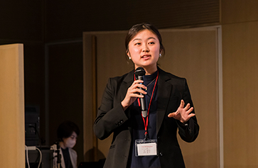 Kanon Mori, wearing a nametag, speaks into a microphone