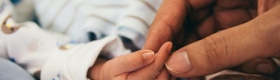 Picture of a hand gently holding a baby’s fingers.