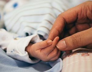 Picture of a hand gently holding a baby’s fingers.