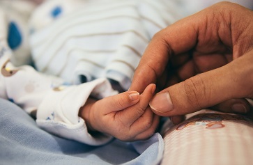 Picture of a hand gently holding a baby’s fingers.