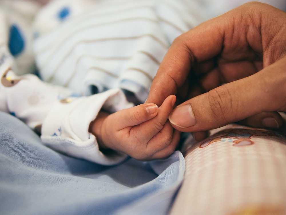 Picture of a hand gently holding a baby’s fingers.