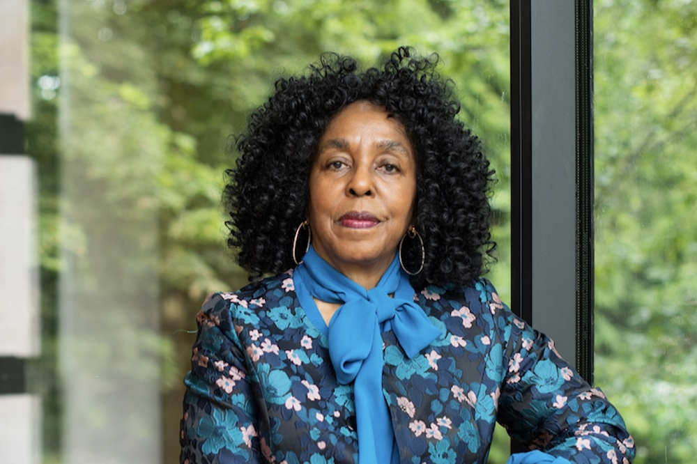 Head-and-shoulders photo of Brenda Stevenson in blue floral dress and blue scarf, with window and trees in background