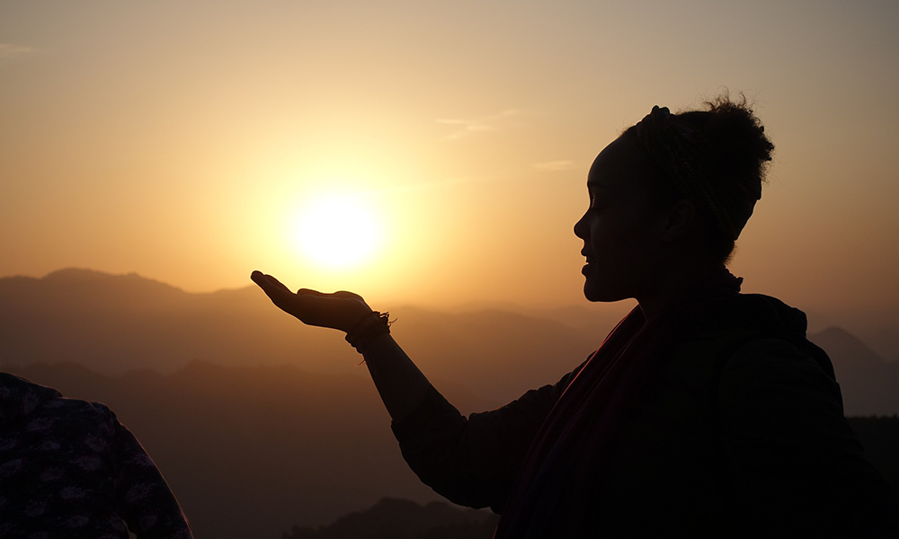 A silhouette of a person with a hand outstretched in front of a golden sunset