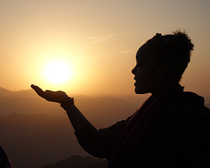 A silhouette of a person with a hand outstretched in front of a golden sunset