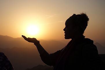 A silhouette of a person with a hand outstretched in front of a golden sunset