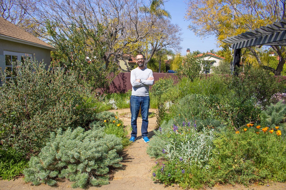 Long shot of Alex Hall standing with arms crossed in his garden