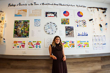 Leah Likin poses in front of a section of the art component of her honors capstone project