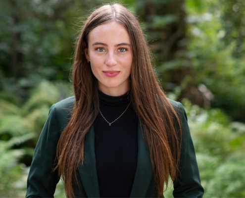 Annabelle Werner in a green blazer, hands clasped before her, with a green plants and stones in the background.