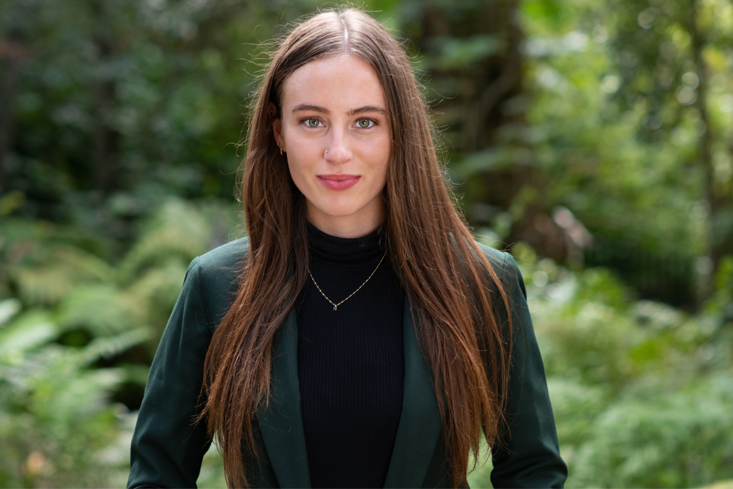 Annabelle Werner in a green blazer, hands clasped before her, with a green plants and stones in the background.