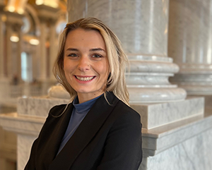 Ariella Gaughan smiling in a black sport coat, with marble columns in the background.