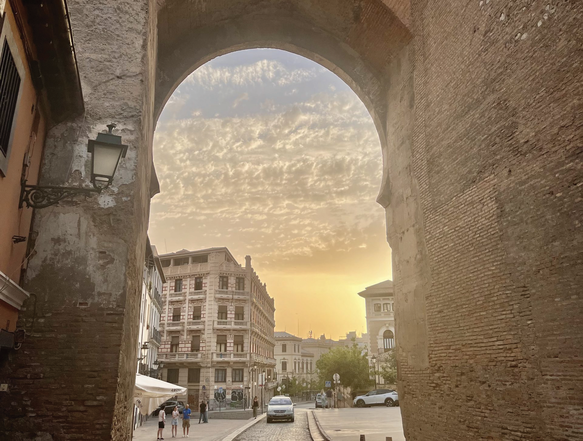A sunset in Granada descending on stone buildings and a cobblestone road.