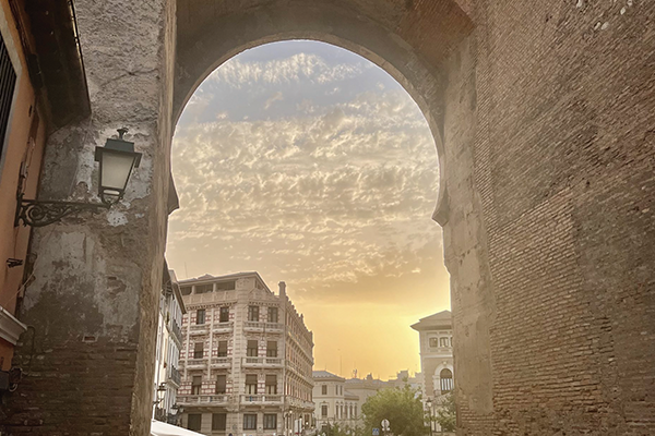 A sunset in Granada descending on stone buildings and a cobblestone road.