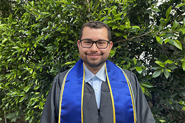 Israel Carrillo wearing a blue and gold graduation sash, with green leaves in the background.