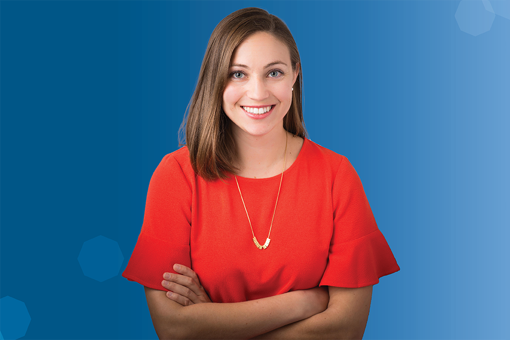 Jessica Cook smiling, wearing a red shirt and gold necklace, against a blue background.