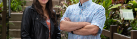 Jordyn Moscoso (left) smiling in a black leather jacket and orange floral shirt, hands clasped before her; Jon Aurnou (right) smiling in a blue checkered short-sleeve collar shirt, arms crossed; concrete steps and green plants in the background.