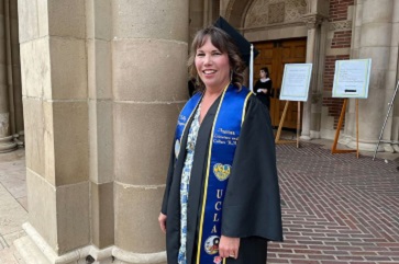 Kelly Kingman smiling, wearing a cap, graduation gown, and a blue sash.