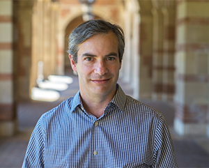 Michael Rothberg in a blue checkered dress shirt, with a walkway lined with stone columns in the background.