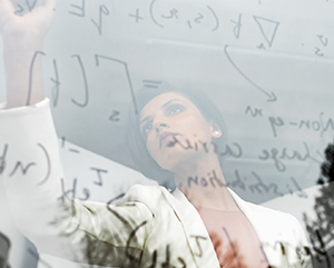 Prineha Narang in a white coat writing equations on a transparent board.