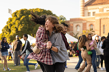 Students laughing and dancing in pairs during the Latinx Welcome event in Wilson Plaza