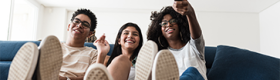 Teenagers sitting close to each other on sofa with their feet on a coffee table; one is holding a TV remote