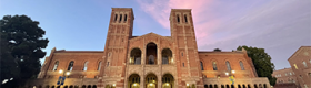 Wide shot of Royce Hall with blue sky and pink clouds, man looking at phone in foreground