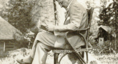 A black and white photograph of William Andrews Clark sitting on a wooden chair somewhere in an outdoor setting with trees in the background.