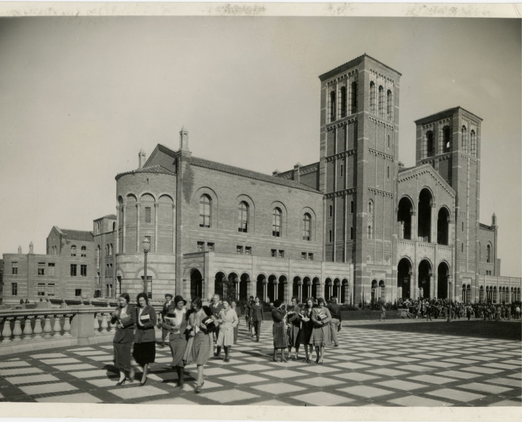A black and white photograph taken in the 1930s depicting students walking across the Royce Hall Terrace, books in hand.