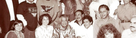 A black and white photograph of César E. Chávez surrounded twenty plus people as they pose for the photograph.