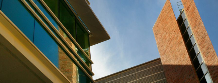 A skyward facing photograph of a building and a blue sky and clouds.