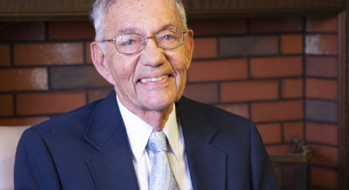 Alumnus Morton La Kretz wearing a blue tie with a white collar shirt and light blue tie, with a red brick wall in the background.