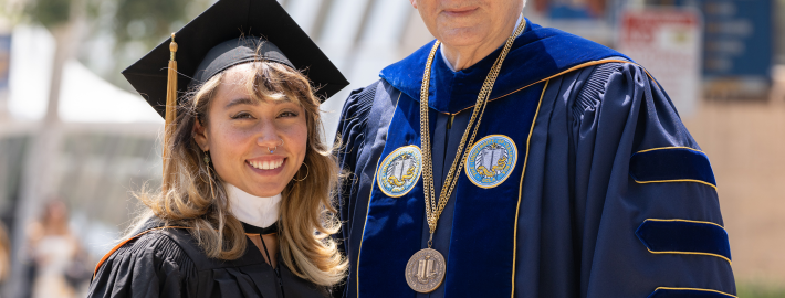 From left to right, gymnast and alumnus Katelyn Ohashi and Chancellor Gene Block in graduation regalia standing outside.