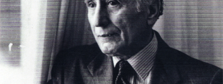 A black and white head and shoulders photograph of Ehsan Yarshater wearing a suit and tie and leaning against a window with curtains. Yarshater (1920–2018), served as the Hagop Kevorkian Professor of Iranian Studies at Columbia University and was a towering figure in the field.