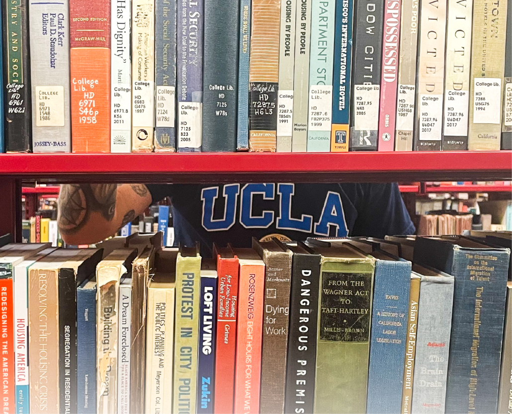 A photograph of a bookshelf with a person wearing a blue shirt that reads "UCLA" in the background.