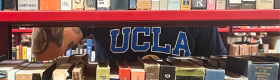 A photograph of a bookshelf with a person wearing a blue shirt that reads "UCLA" in the background.