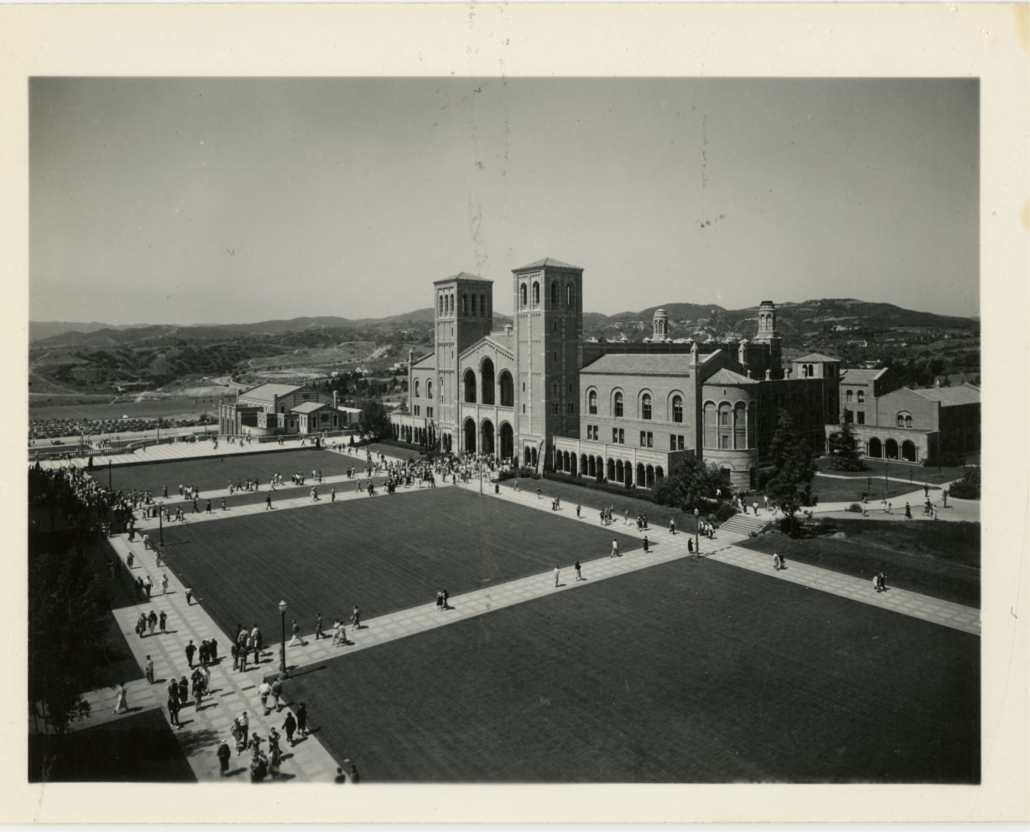 A black and white photograph of Royce Hall and students walking on a sidewalk, going to and from class.